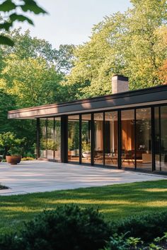 a modern house with glass walls in the middle of a yard and trees surrounding it