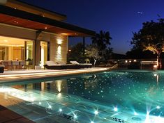 an outdoor swimming pool at night with lights shining on the water and furniture in the background