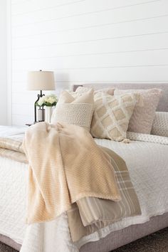 a bed with pillows and blankets on top of it next to a lamp in a room