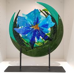 a blue flower sitting on top of a green object in a white room with black stand