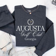 Fore! Calling all golf lovers - get ready to tee off in style with our Augusta Georgia Golf Sweatshirt! This cozy sweatshirt features a distressed serif font and a circle graphic representation of a golf course in the iconic Masters colors. The design is sure to score a hole-in-one with its vintage vibe and eye-catching visuals. Made from quality materials, this sweatshirt is perfect for hitting the links or chilling at the clubhouse. So, swing into action and add this Augusta Georgia Golf Sweatshirt to your collection today! Ideal for any situation, a unisex heavy blend crewneck sweatshirt is pure comfort. These garments are made from polyester and cotton. This combination helps designs come out looking fresh and beautiful. The collar is ribbed knit, so it retains its shape even after was State Crewneck, Augusta Golf, Golf Sweatshirt, Circle Graphic, Augusta Georgia, Club Sweatshirts, Golf Lover, Gifts For Golfers, Golf Tournament