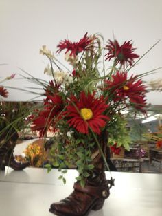 a vase filled with red and white flowers on top of a table next to a pair of cowboy boots