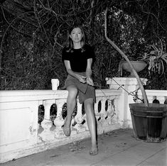 black and white photograph of a woman sitting on a wall next to a potted plant