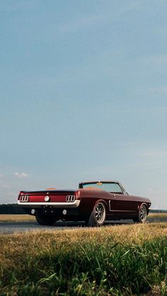 an old car is parked on the side of the road in front of some tall grass