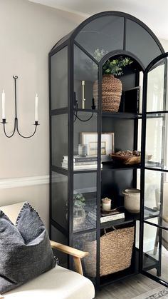 a living room filled with furniture and a tall glass case next to a window on the wall