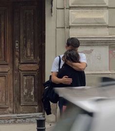 two people hugging each other in front of a building