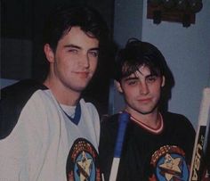 two men standing next to each other holding baseball bats and wearing shirts with emblems on them