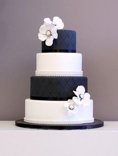 a three tiered wedding cake with white flowers on the top and black trimmings