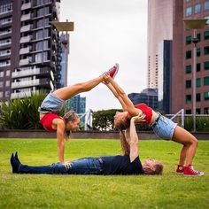 two people doing handstands on the grass in front of tall buildings