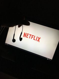 a hand holding a cell phone with the netflix logo on it in front of a computer screen