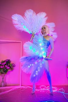 a woman is dressed up as a fairy with lights on her body and feathers around her legs