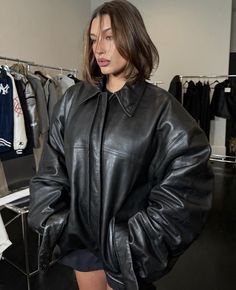 a woman standing in front of a rack of clothes wearing a black leather jacket and shorts