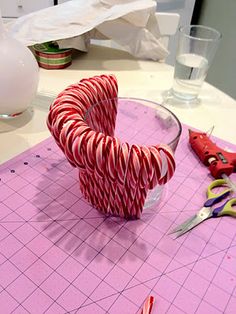 candy canes in a bowl sitting on top of a cutting board next to scissors