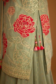 the back of a woman's green dress with red flowers and tassels