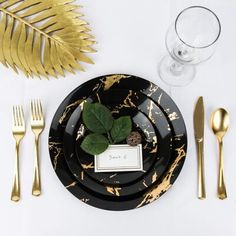 a place setting with gold and black plates, silverware, and a green leaf