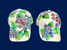 Blend in with the flowers! White 100% cotton cap is painted all over with hydrangea flowers in variegated shades of blue, purple and pink, with the occasional green leaf. Optional butterfly or dragonfly or ladybug. 100% cotton cap with adjustable back strap.   Each cap is hand painted one at a time with artist-quality, non-toxic acrylic paints which are permanent once dry. Design will not wash out or peel off in the wash. Get caught in the rain? Your hydrangeas will still be there; they'll just be all wet Cold water wash, line dry. Chlorine bleach may be used without harming the painting. Purple Hat For Spring As A Gift, Purple Hat For Spring Gift, Purple Hat As A Spring Gift, Purple Spring Gift Hats, Caught In The Rain, Hydrangea Flowers, Bleu Violet, Flowers White, Hydrangea Flower