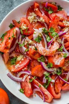 a white bowl filled with tomatoes, onions and feta cheese on top of a table