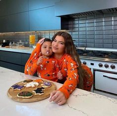 a woman and her child are sitting in front of a cutting board with food on it