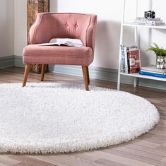 a pink chair sitting on top of a wooden floor next to a book shelf and white rug