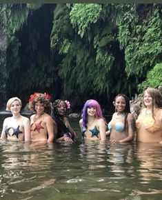 a group of women in bikinis are standing in the water near a waterfall and trees