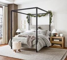 a bedroom with a four poster bed and white walls, hardwood floors, two lamps on either side of the bed