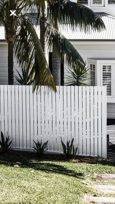 a white picket fence in front of a house with palm trees on the lawn and sidewalk