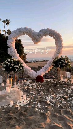 an image of a heart made out of flowers and candles on the beach with palm trees in the background