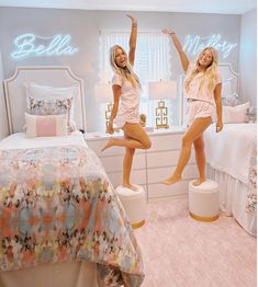 two beautiful young women standing next to each other in front of a bed with lights on it