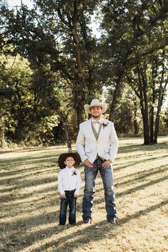 a man in a white suit and tie standing next to a little boy wearing a cowboy hat