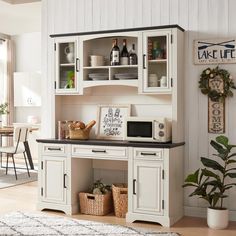 a white hutch with black counter top and shelves on the wall next to a potted plant