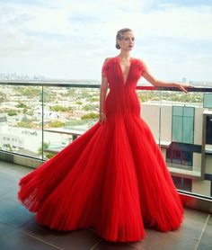 a woman in a long red dress standing on a balcony with her arms out to the side