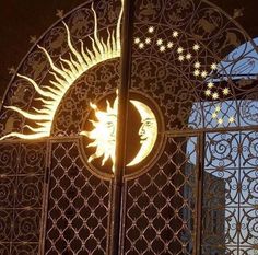 the sun and moon are lit up in front of a decorative iron gate at night