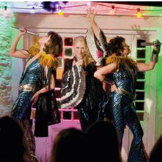 three women in sequins are dancing on stage with their hands up to the ceiling