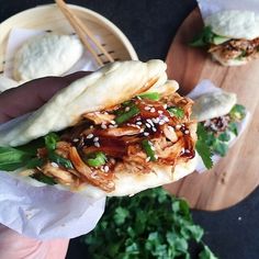 a person holding up a sandwich with meat and veggies on it in front of some bread