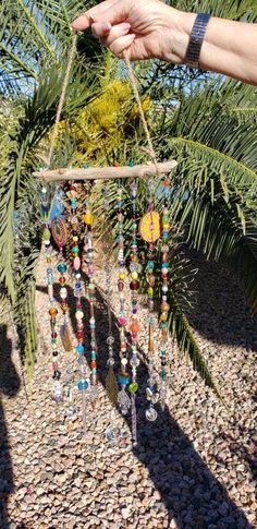 a person holding up a wind chime hanging from a palm tree in the sun