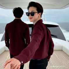 two people are holding hands on a boat in the ocean, one is wearing sunglasses and the other wears a maroon shirt