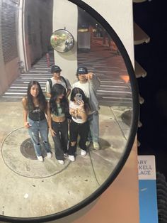 a group of young people standing next to each other in front of a round mirror