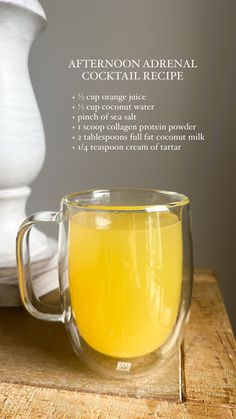 a glass mug filled with orange juice on top of a wooden table next to a white pitcher