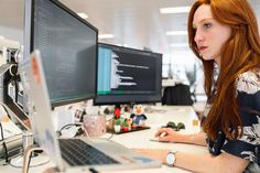 a woman sitting at a desk in front of two computer monitors