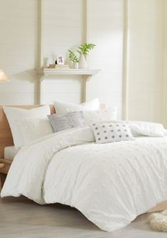 a bed with white comforter and pillows in a room next to a lamp on the wall