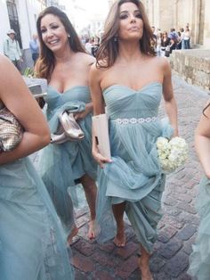 three women in blue dresses are walking down the street with one woman holding a purse