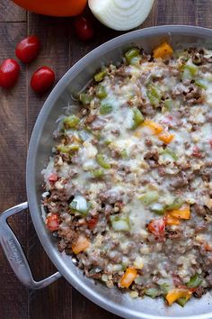 a pan filled with food sitting on top of a wooden table next to tomatoes and onions