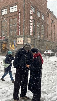 two people standing in the snow on a city street