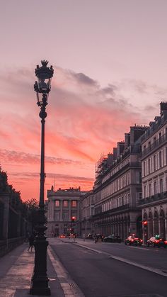 a street light sitting on the side of a road next to tall buildings at sunset