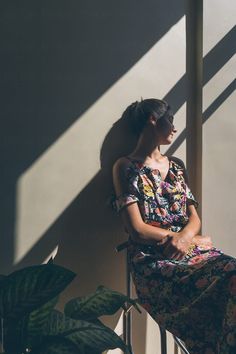 a woman sitting on a chair in the sun by a plant with long shadows behind her