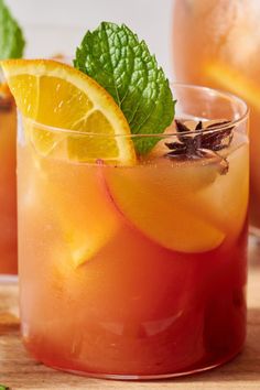 two glasses filled with lemonade and mint on top of a wooden table next to sliced oranges