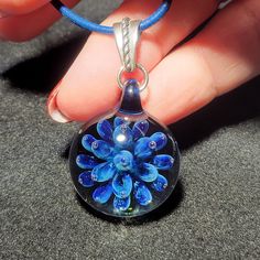 "This is one of my second favorite pendants that I currently have in stock. On a clear base is a beautiful royal blue flower implosion that sparkles from a color called stardust. I make each handmade implosion pendant using a blowtorch and Borosilicate glass in my studio. I love the depth and sometimes, trapped bubbles I can achieve with these pendants. This design reminds me of a lotus blossom trapped in glass. Each of these pendants are one of a kind that I create out of molten glass. I only u Blue Glass Flower Shaped Jewelry, Clear Glass Flower Jewelry, Blue Flower Shaped Glass Jewelry, Blue Flower-shaped Glass Jewelry, Blue Round Recycled Glass Jewelry, Blue Recycled Glass Round Jewelry, Unique Blue Flower Pendant Jewelry, Blue Recycled Glass Jewelry As Gift, Blue Murano Glass Round Jewelry