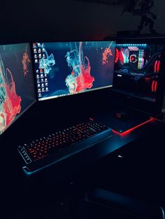 two computer monitors sitting next to each other on top of a black desk with red and blue lights