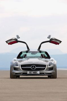 a mercedes sls with its doors open on the beach in front of some mountains