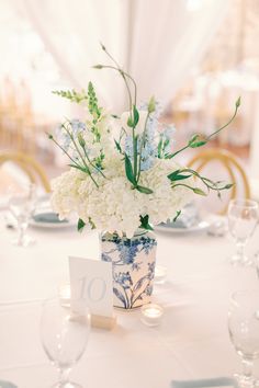 a vase with white flowers and greenery on a table set for an elegant dinner